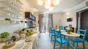 A modern kitchen with a dining area, featuring a central island with kitchenware, a built-in oven, and a flat-screen TV mounted above the island.