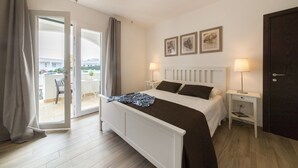 A bedroom with a bed, bedside tables, a door, and a view through a sliding glass door to an outdoor area.