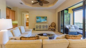 A spacious living room with a large sofa set, a ceiling fan, a painting, and a view through a glass door to an outdoor seating area. - Prentiss Pointe Condo - 3 bedroom, 2 bath, 2-Floor Condo in Ft Myers (Fort Myers)