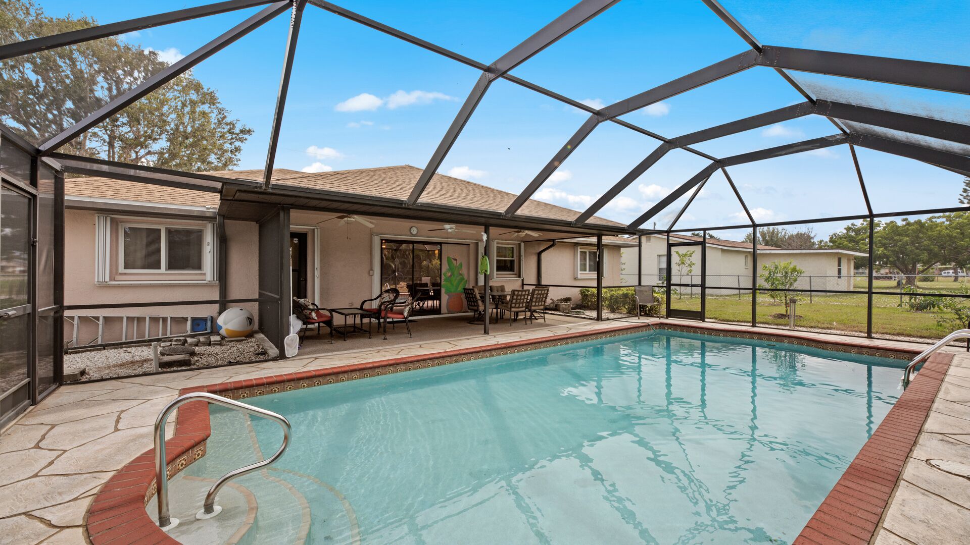 A covered swimming pool with a patio area, a covered seating area, and a view of the surrounding neighborhood.