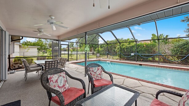 A covered outdoor area with a pool, wicker furniture, and a view of the surrounding landscape.