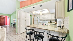 A kitchen with white cabinets, a granite countertop, and black bar stools.