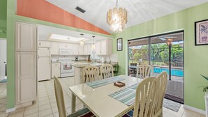 A modern kitchen with white cabinets, a dining area with a table and chairs, and a view of a swimming pool through large windows.