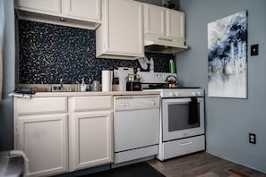A kitchen with white cabinets, a dishwasher, an oven, and a backsplash with a speckled pattern.