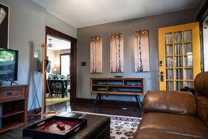 Un salon avec un canapé en cuir marron, un meuble de rangement en bois et un téléviseur posé sur un support.