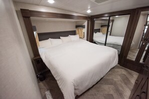 Une chambre d’hôtel avec un grand lit, une tête de lit en bois, un miroir et une petite table de chevet.