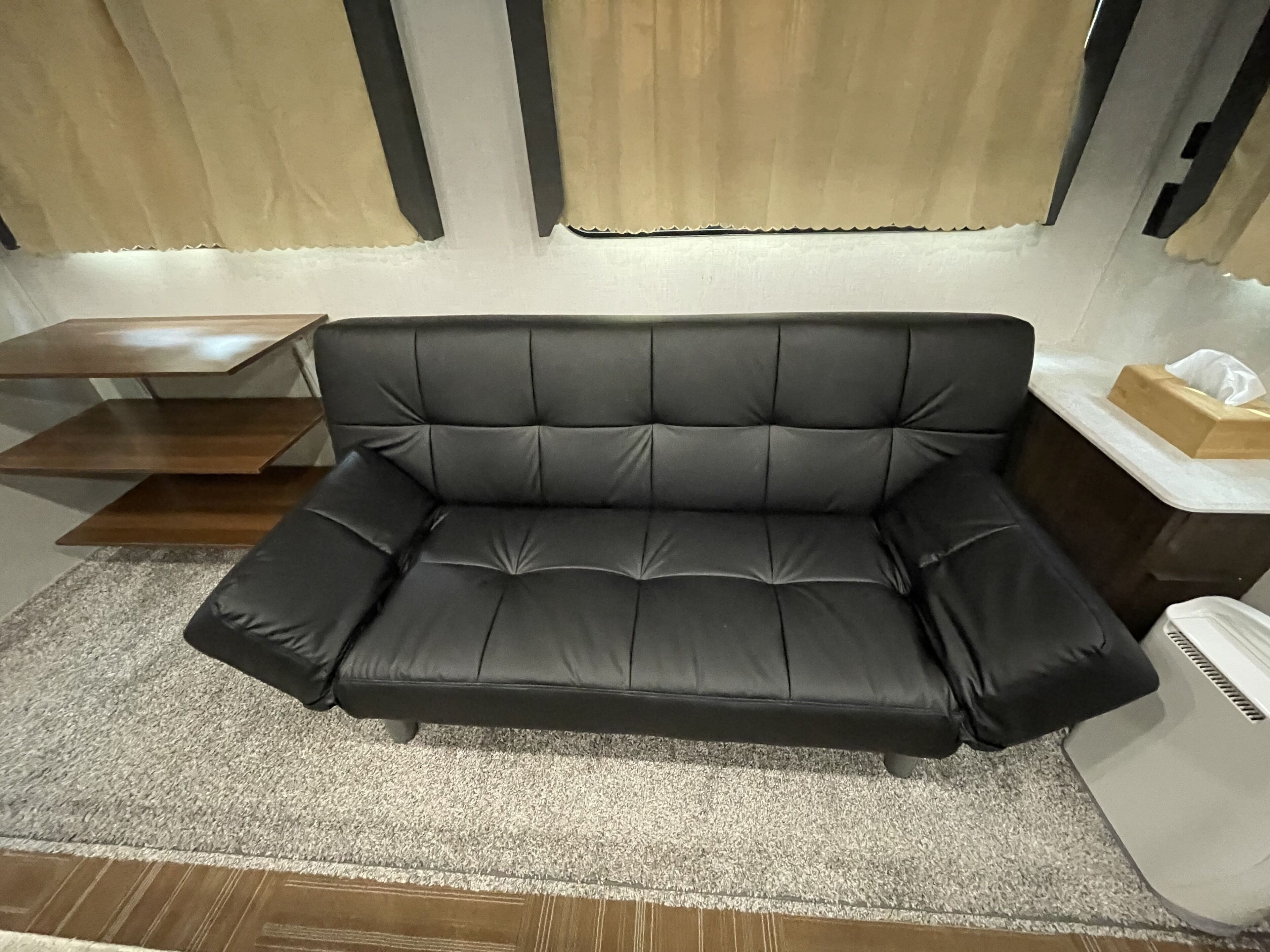 Um sofá de couro preto com uma mesinha de madeira e uma mesinha de cabeceira branca com um estojo de lenços.