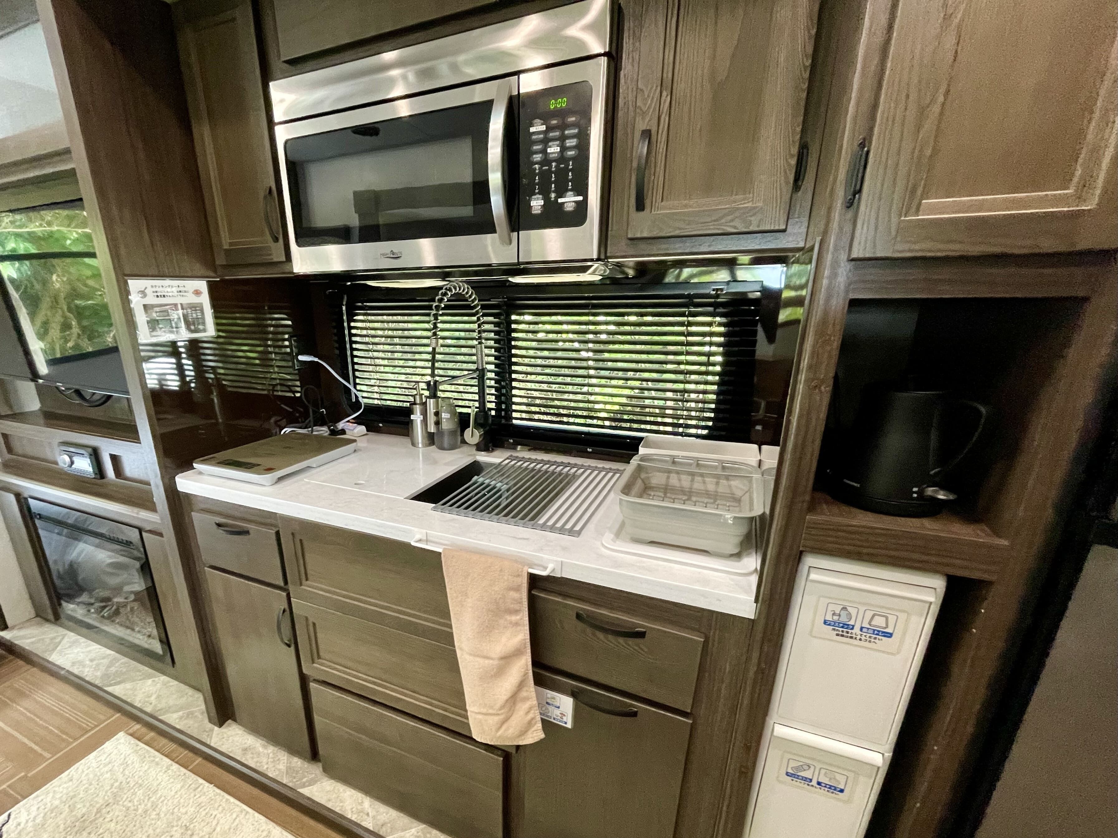 A compact kitchenette with a stainless steel microwave, a sink with a faucet, a kettle, and a coffee maker.