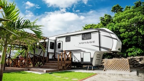 A white RV with "VOYAGE" written on it, parked in a grassy area with a wooden deck and steps leading up to it. - Logasis Ishigaki Nosoko Villa (Ishigaki)