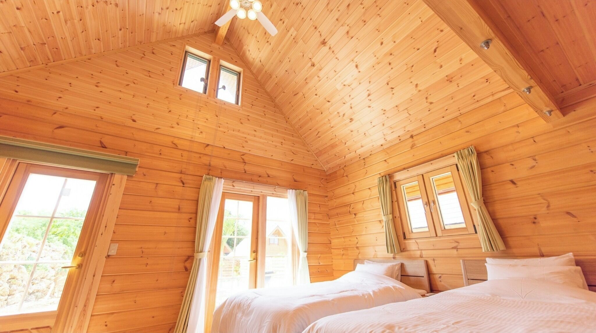Een houten kamer met twee bedden, een plafondventilator en grote ramen.