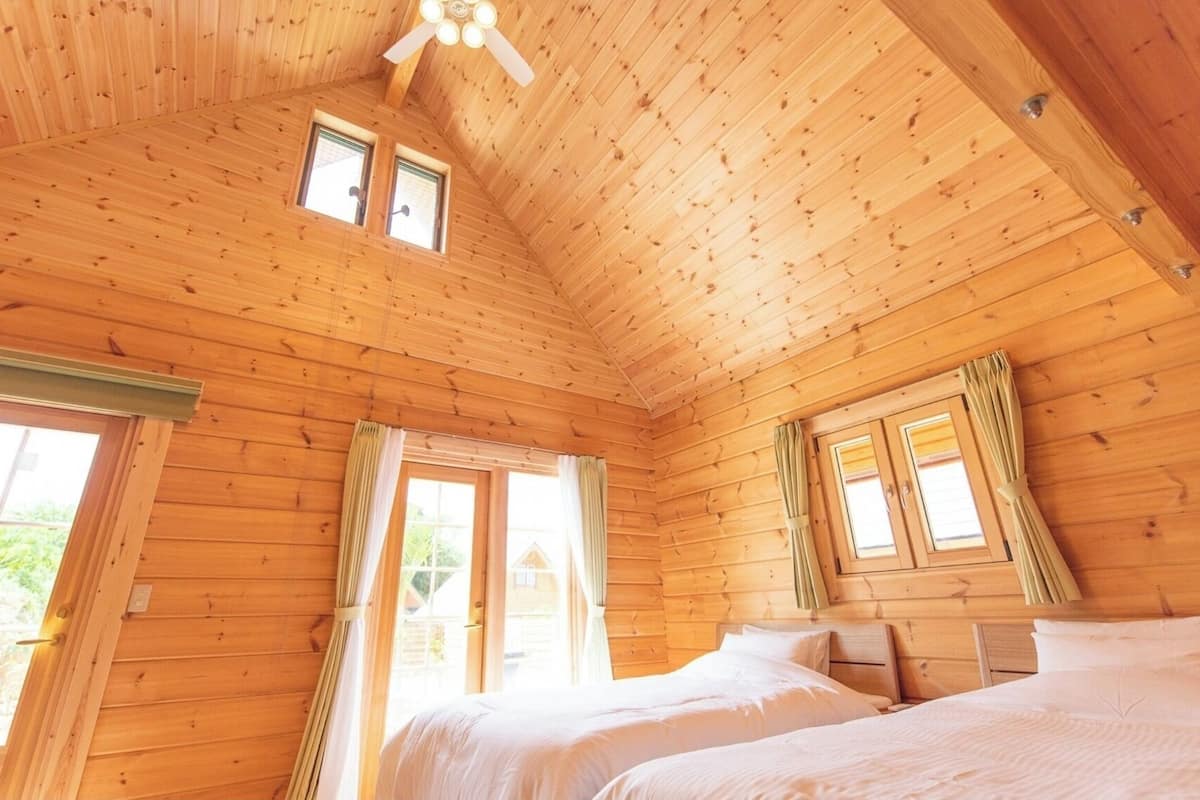 Een houten kamer met twee bedden, een plafondventilator en grote ramen.
