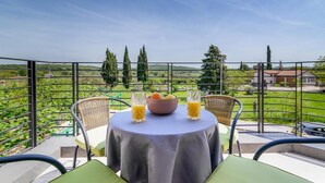 A balcony with a table set for two, two glasses of orange juice, a bowl of fruit, and a view of the countryside.