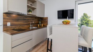 A modern kitchen with a wooden countertop, a built-in sink, and a small shelf. There is a dining area with a chair and a table, and a TV mounted on the wall.