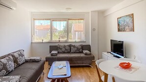 A living room with a sofa, a coffee table, a TV, and a window with a view of buildings.