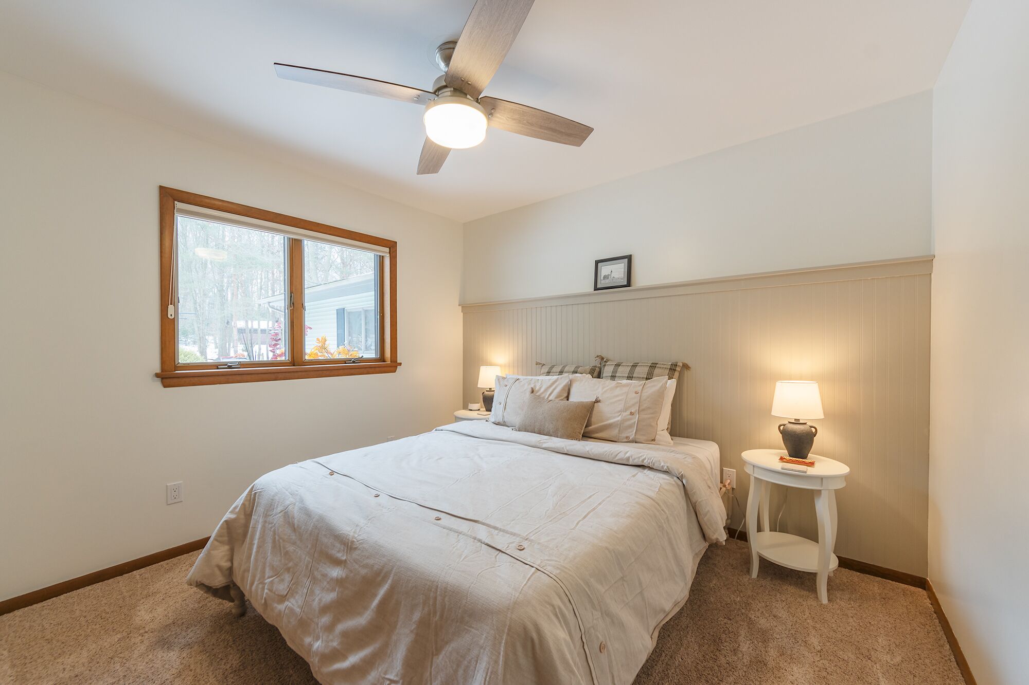 A bedroom with a bed, a ceiling fan, a window, and a bedside table with a lamp.