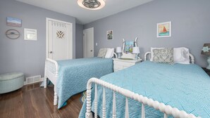 Een slaapkamer met twee bedden, een witte plafondventilator en een deur met decoratieve kruizen.