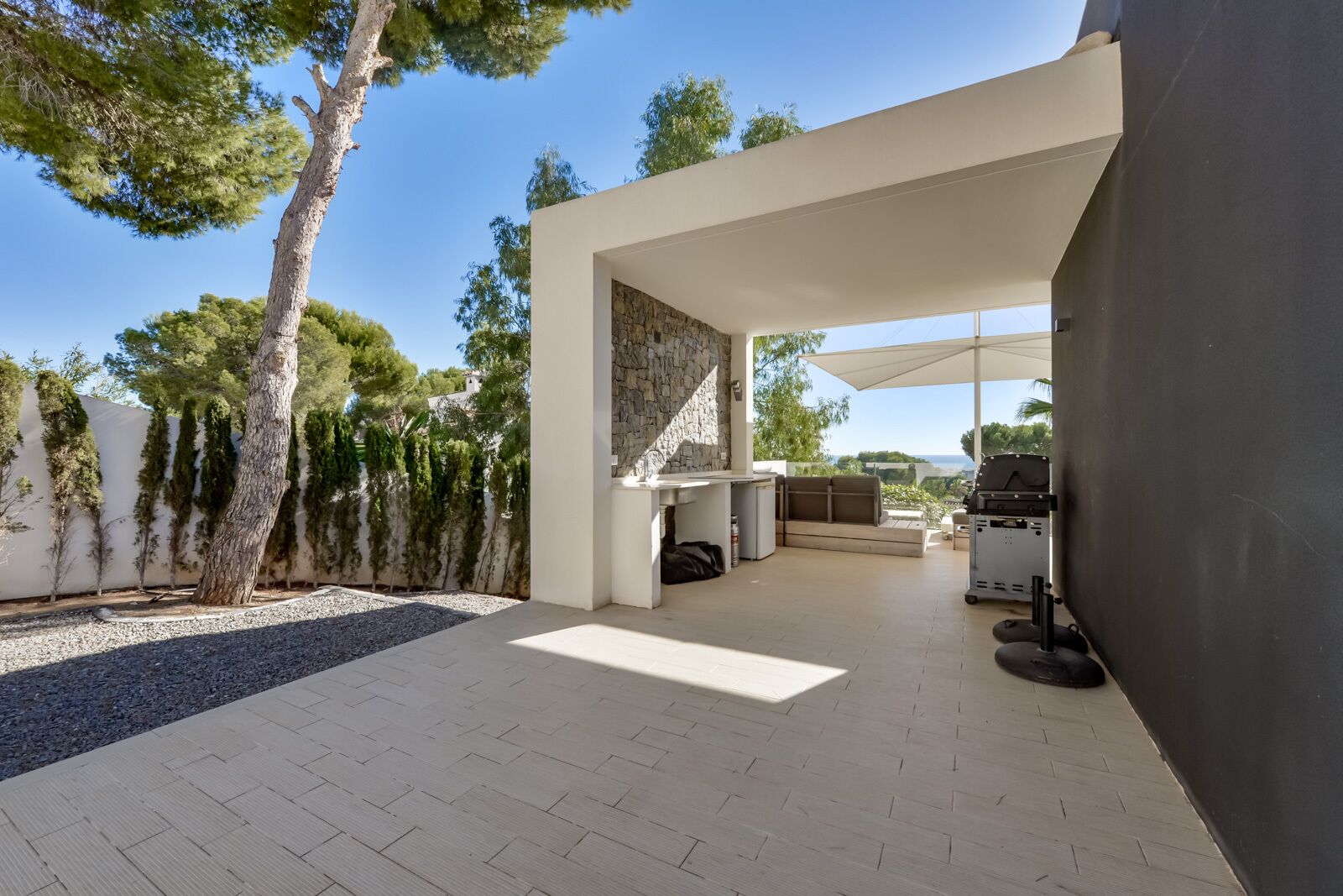 Un patio moderno al aire libre con pared de piedra, zona de barbacoa y un conjunto de asientos.