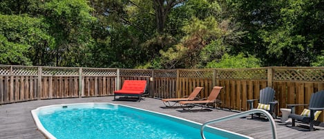 A rectangular swimming pool with a wooden deck, surrounded by a wooden fence and trees.