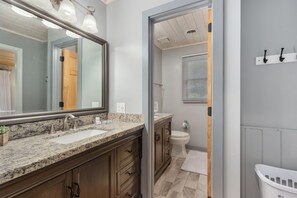 A bathroom with a granite countertop, a double sink, a large mirror, and a toilet.