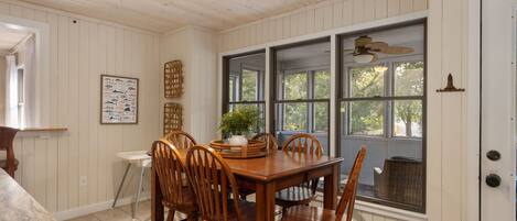 A dining area with a wooden table and chairs, a window with a view of trees, and a ceiling fan.