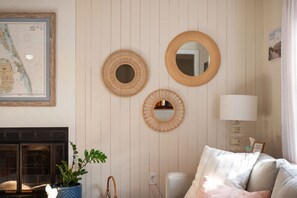 A room with three wall-mounted mirrors, a framed map, a fireplace, a potted plant, and a bed with pillows.