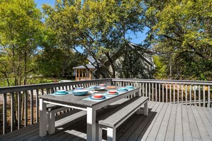 An outdoor dining area with a wooden deck, a table set with plates and bowls, and a gazebo in the background. - Coastal Hideaway: Private Pool, Walk to the Beach, Perfect for Families (Southern Shores)