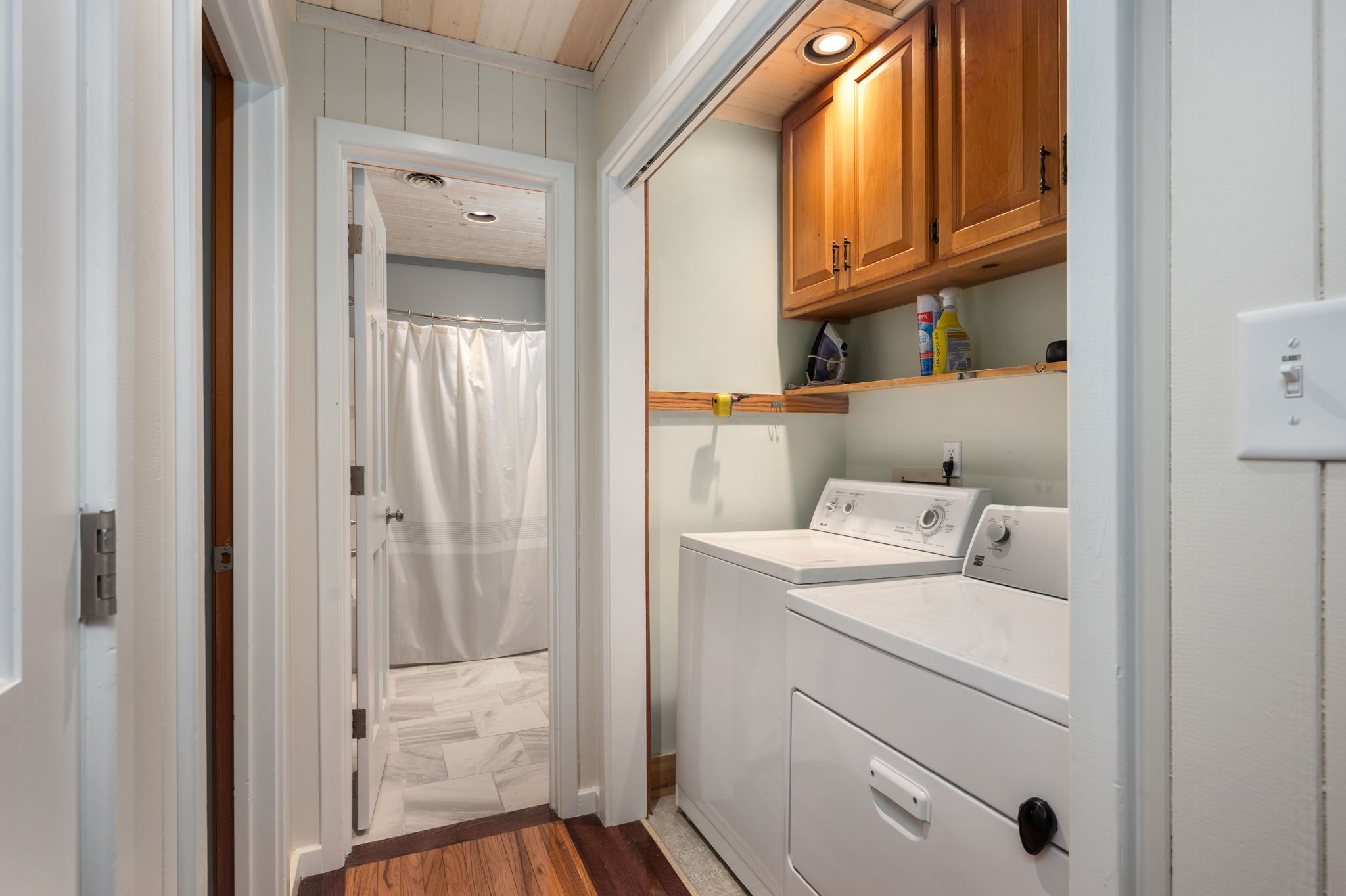 A laundry room with a washing machine, dryer, and wooden cabinets.