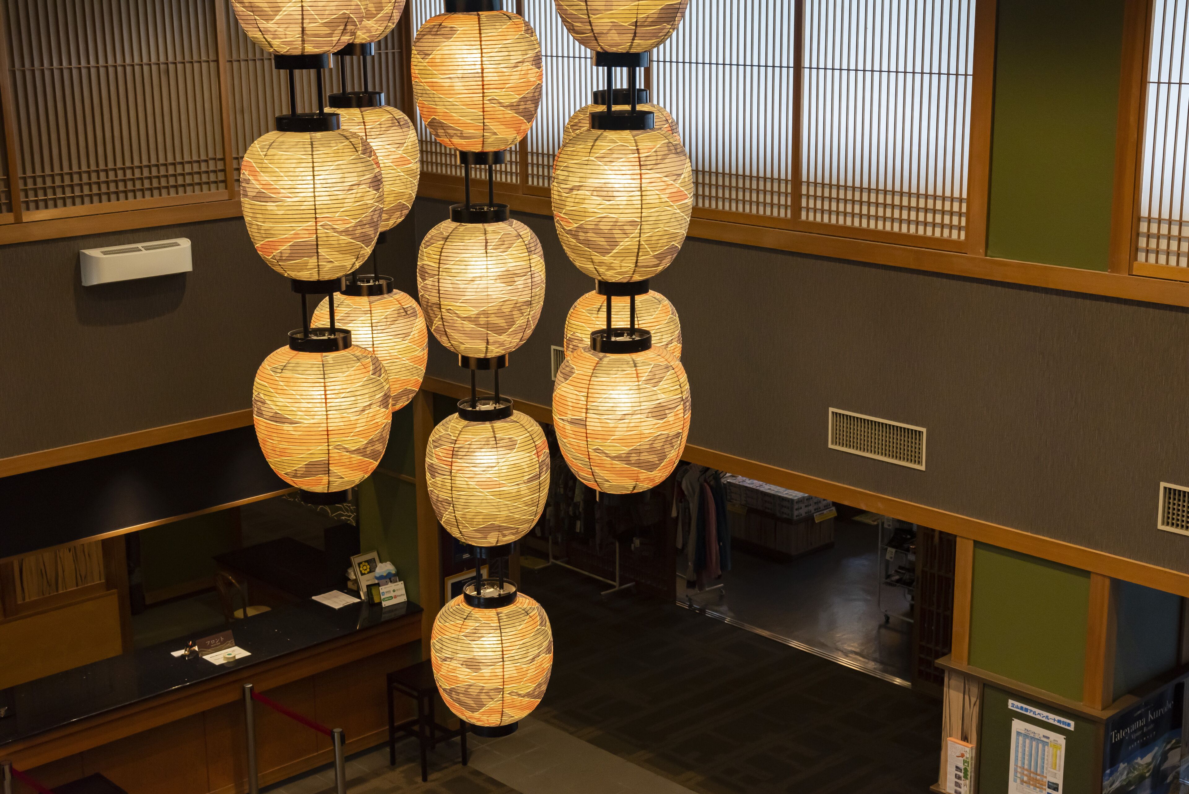 A hotel lobby with multiple hanging paper lanterns, a reception desk, and a view of the interior space.