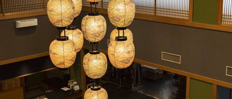 A hotel lobby with multiple hanging paper lanterns, a reception desk, and a view of the interior space.