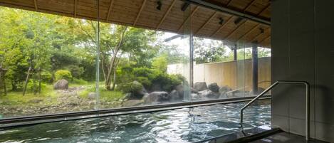 A hot spring area with a wooden ceiling, a glass wall, and a metal railing.