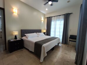 Quarto de hotel com cama, mesas de cabeceira, ventoinha no teto e vista para o exterior através de cortinas.