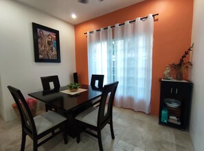 A dining area with a table and chairs, a framed picture on the wall, and a window with curtains.