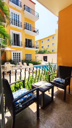 Zona de piscina con asientos al aire libre y vistas a un edificio amarillo con balcones.