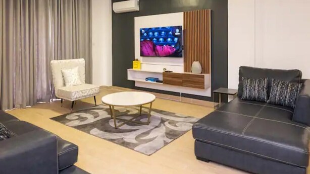 A modern living room with a large flat-screen TV, a sofa, a chair, and a coffee table. - Canalily Apt

 (Lekki)