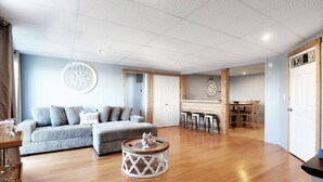 A spacious living area with a sofa, round coffee table, and a dining area with stools. - Chain O` Lakes Beach Penthouse Sunset View and Boat Dock (Ingleside)