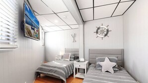 A bedroom with two beds, a TV, a ship's wheel decoration, and a window with blinds. - Chain O` Lakes Beach Penthouse Sunset View and Boat Dock (Ingleside)