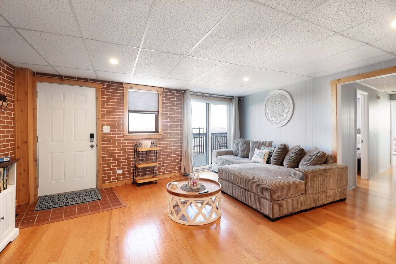 A living room with a brick wall, a white door, a sofa, a coffee table, and a window with a view.