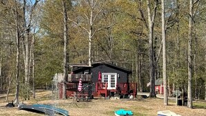 A cabin by a lake with a dock, a boat, and a fountain.