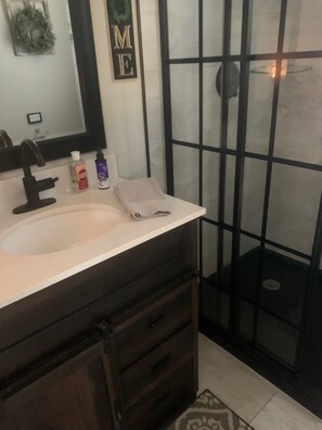 Un baño con lavamanos blanco, tocador de madera oscura, espejo y ducha con puerta de vidrio.
