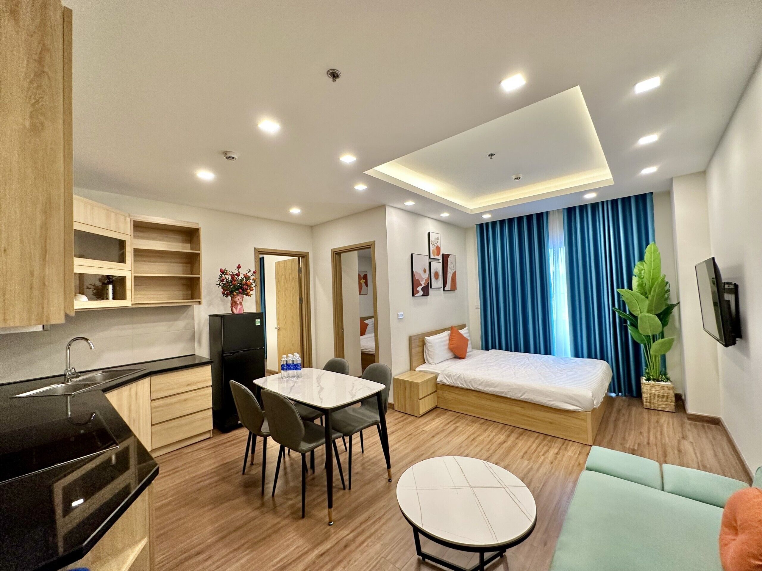 Habitació d'hotel moderna amb llit, taula de menjador, zona de cuina i finestra gran amb cortines.