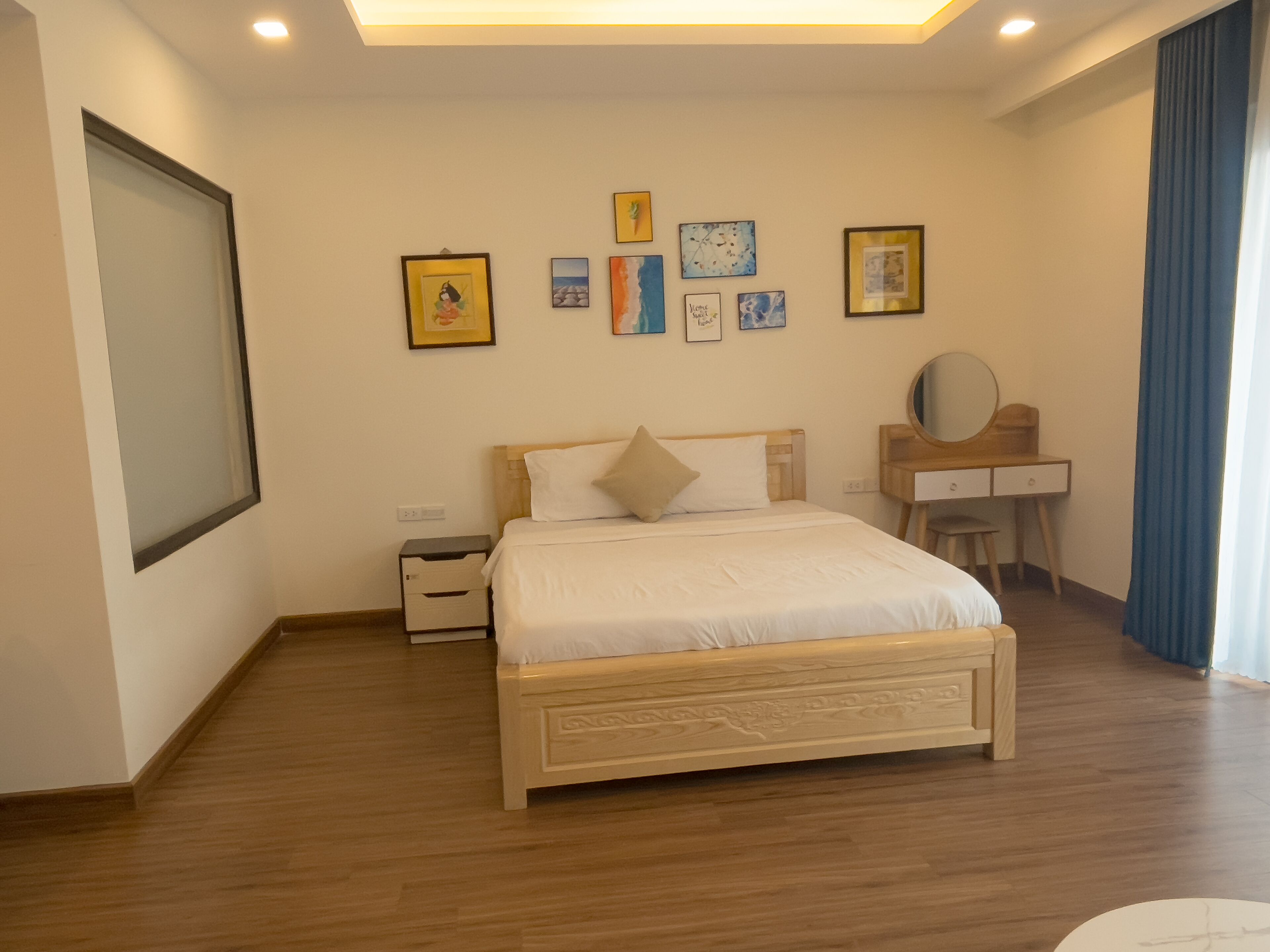 Quarto com cama de madeira, escrivaninha, cadeira e espelho. Há quadros nas paredes.