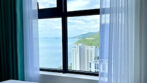 A hotel room with a large window offering a view of a cityscape and hills. - FLC Sea Tower -  An Phat Apartment  (Quy Nhon Nam)