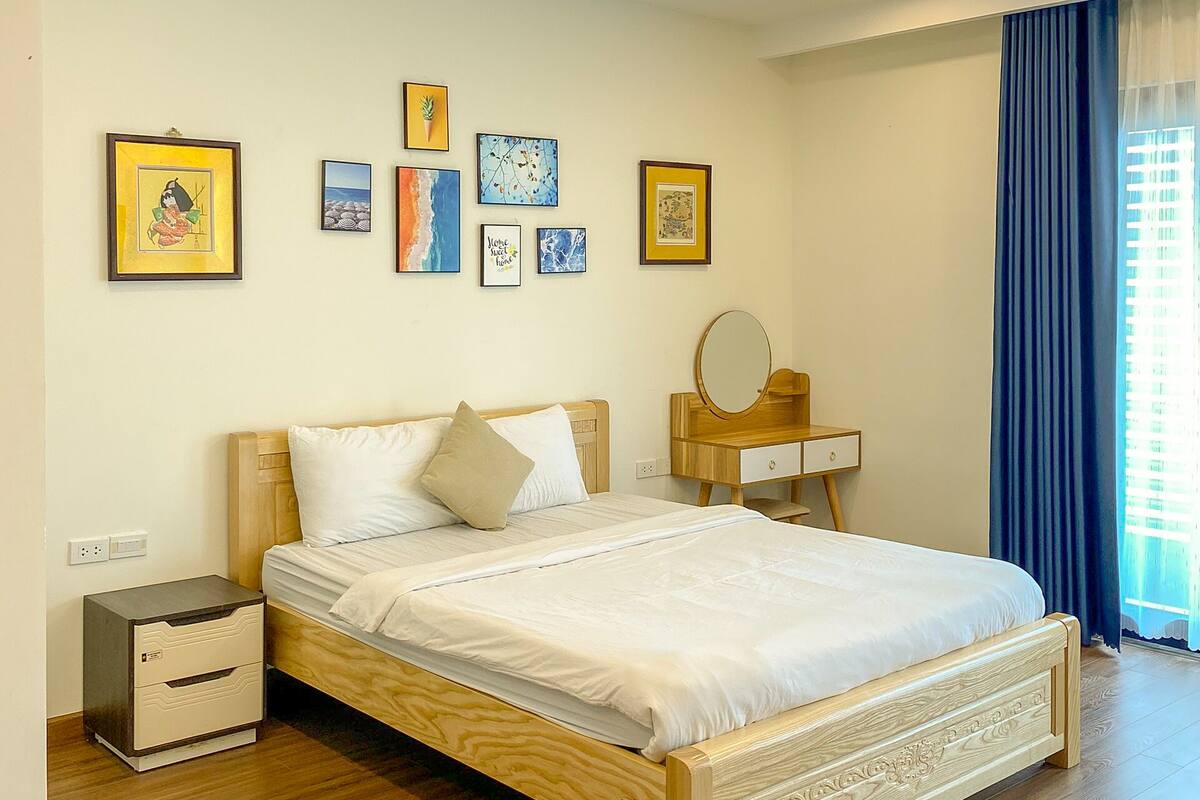 A modern hotel room with a wooden bed, a bedside table with a mirror, and a wall with framed artwork.