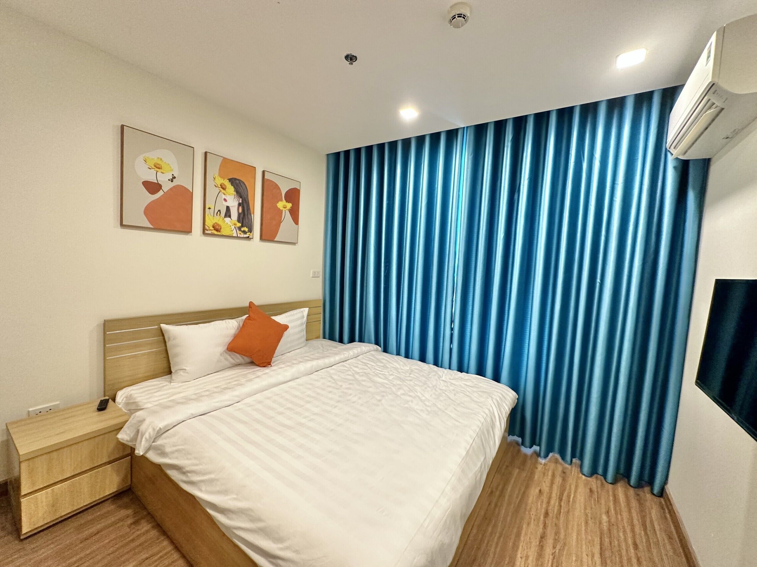 Une chambre d’hôtel avec un lit, une table de chevet, un téléviseur fixé au mur et une fenêtre avec des rideaux bleus.