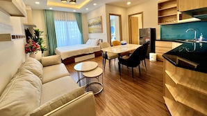 A modern hotel room with a bed, sofa, dining table, chairs, and a kitchen area. - FLC Sea Tower -  An Phat Apartment  (Quy Nhon Nam)