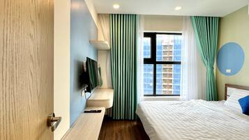 A modern hotel room with a wooden floor, a bed with white bedding, a mounted TV, and a window with curtains.