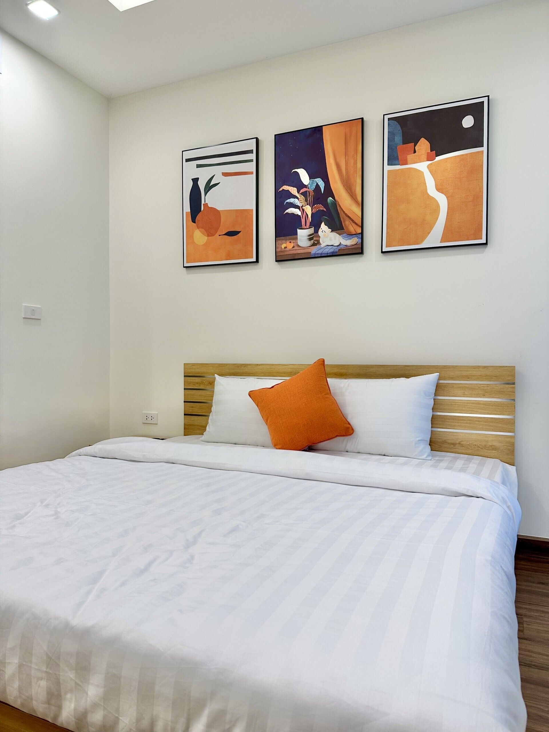 A bedroom with a bed, white bedding, and three framed artworks on the wall.