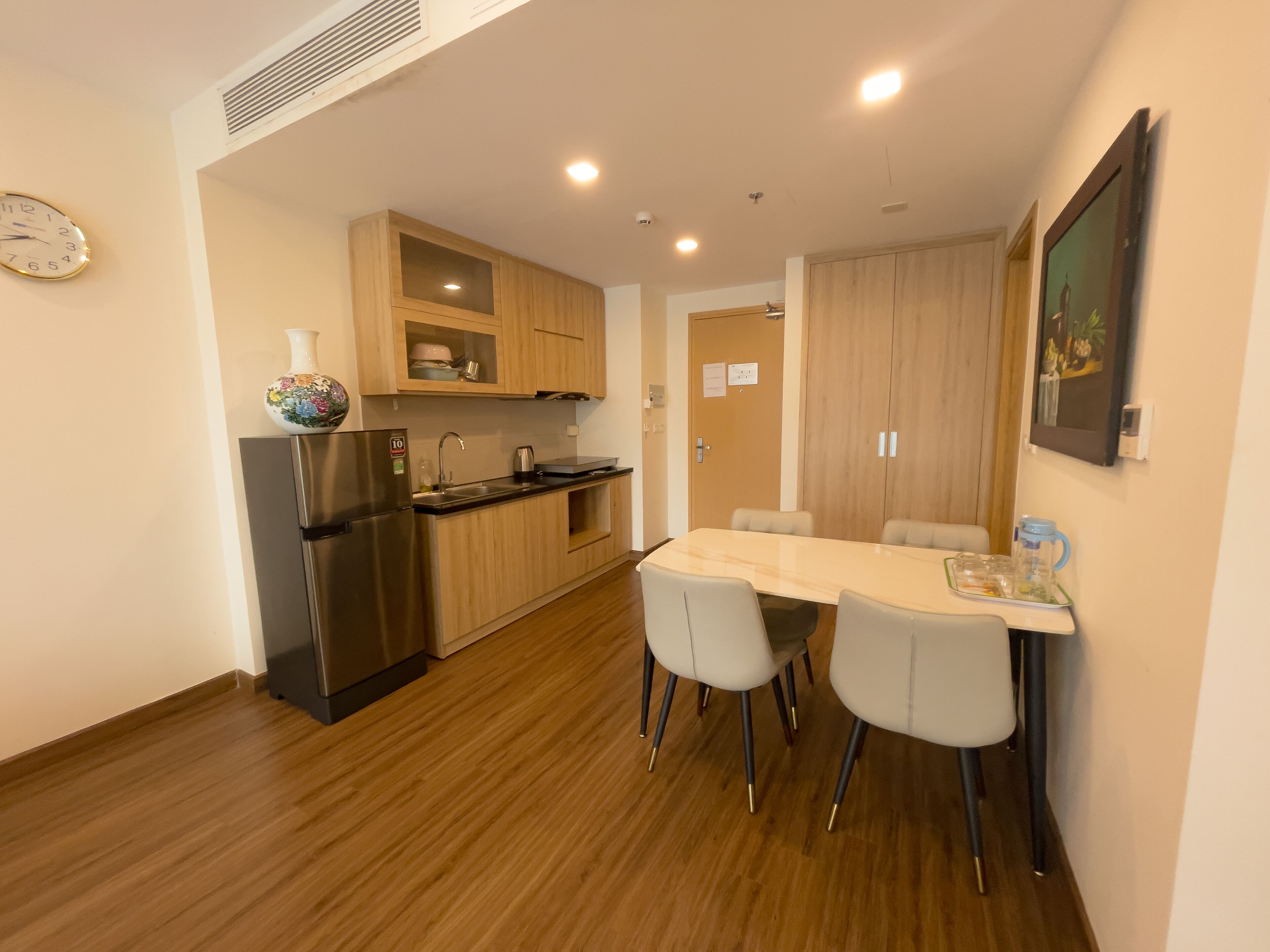 Une cuisine moderne avec des meubles en bois, un réfrigérateur en acier inoxydable et un coin repas comprenant une table et des chaises blanches.