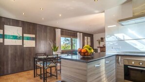 A modern kitchen with a central island, a dining area with chairs, and a large window providing natural light. - Son Alcaines Sineu by Interhome (Sineu)