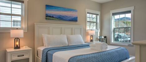 A bedroom with a bed, nightstands, a ceiling fan, and a painting on the wall.